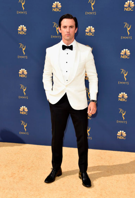 Milo Ventimiglia luciendo un traje de chaqueta blanca con pantalón, zapatos y moño negros en la premiación Emmy 2018.